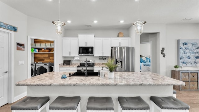 kitchen with washer and clothes dryer, a center island with sink, decorative light fixtures, and appliances with stainless steel finishes