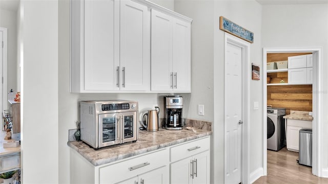 interior space featuring washer / dryer, light wood-type flooring, white cabinetry, and light stone counters