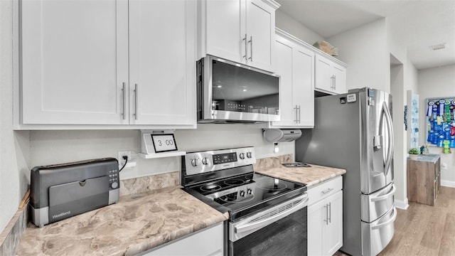 kitchen featuring white cabinets, light wood-type flooring, stainless steel appliances, and light stone counters