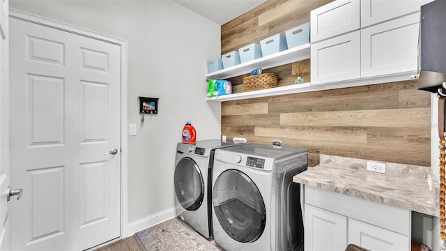 clothes washing area featuring washing machine and clothes dryer, wood walls, and cabinets