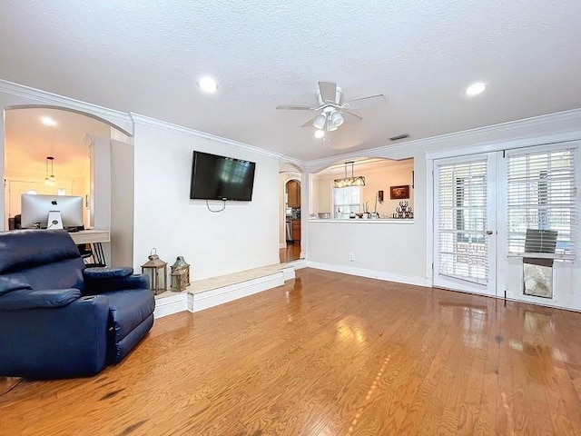 living room with ceiling fan, wood-type flooring, a textured ceiling, and ornamental molding