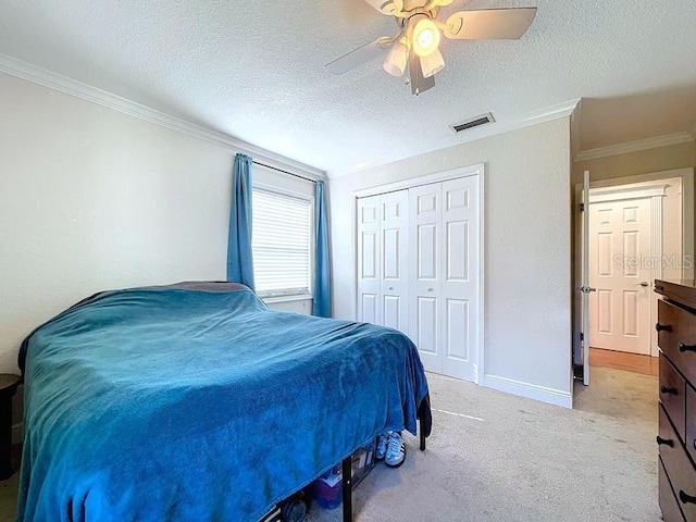 carpeted bedroom with ceiling fan, a closet, a textured ceiling, and ornamental molding