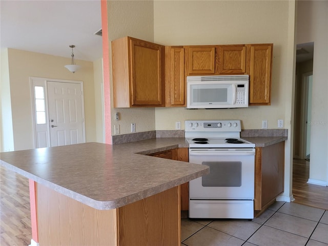 kitchen with light tile patterned floors, white appliances, kitchen peninsula, and hanging light fixtures