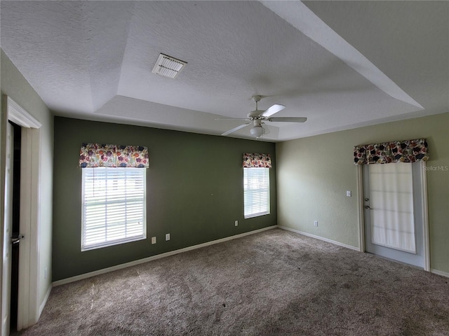 carpeted empty room with a wealth of natural light, a textured ceiling, a raised ceiling, and ceiling fan