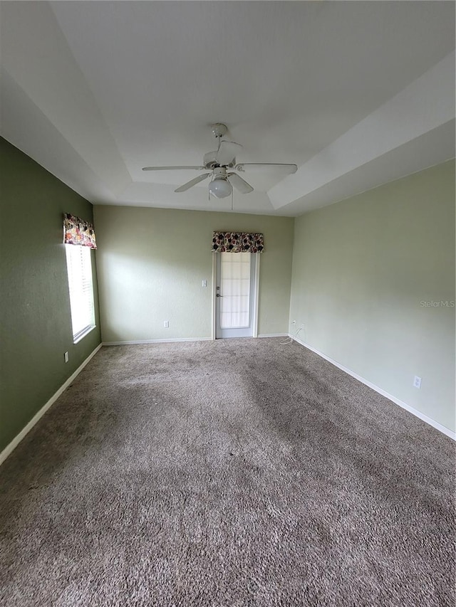 empty room featuring carpet, a tray ceiling, and ceiling fan