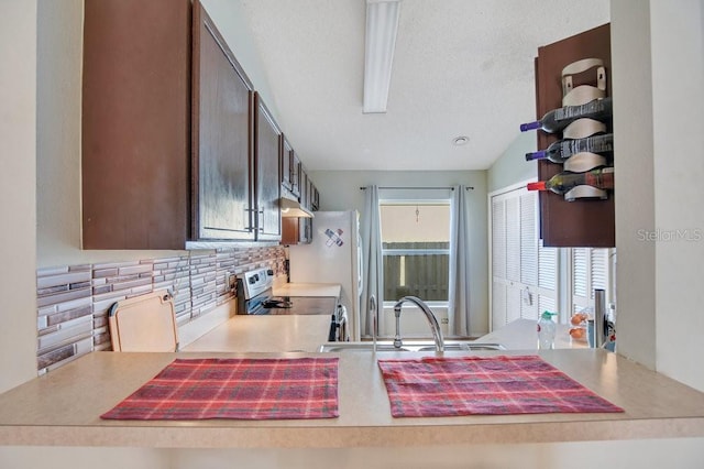 kitchen with backsplash, dark brown cabinets, stainless steel electric range, vaulted ceiling, and sink