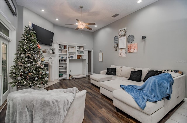 living room featuring hardwood / wood-style floors, ceiling fan, a towering ceiling, and a textured ceiling