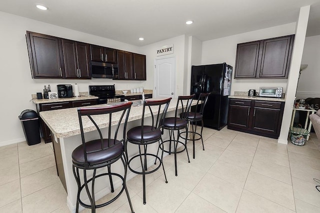 kitchen featuring a kitchen breakfast bar, light tile patterned floors, a kitchen island with sink, and black appliances