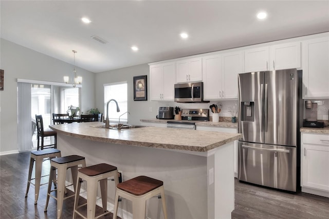 kitchen featuring pendant lighting, lofted ceiling, a center island with sink, white cabinets, and appliances with stainless steel finishes