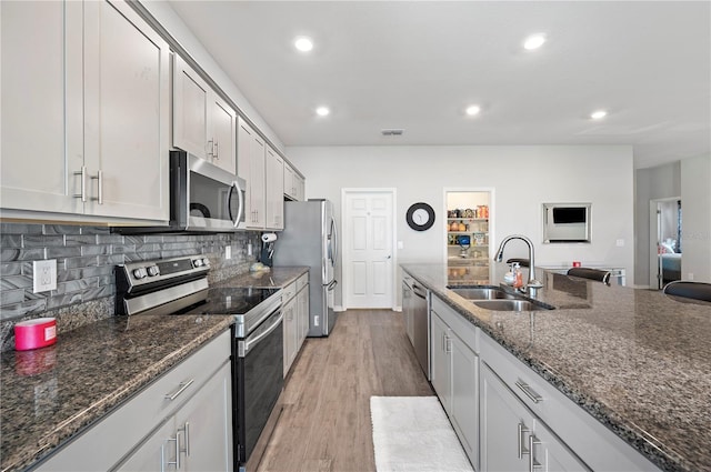 kitchen with sink, dark stone countertops, light hardwood / wood-style floors, white cabinets, and appliances with stainless steel finishes