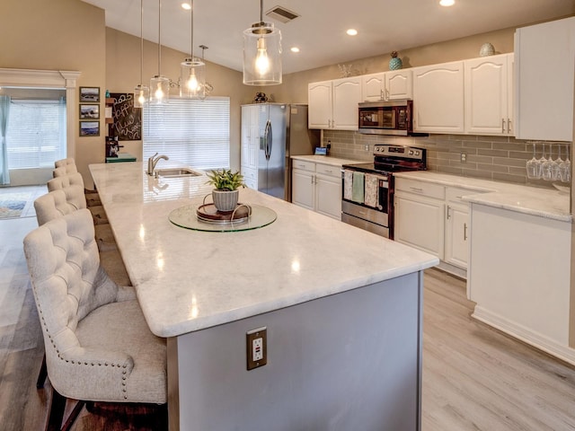 kitchen featuring white cabinets, stainless steel appliances, hanging light fixtures, and an island with sink