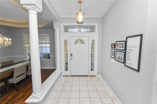 tiled foyer entrance with plenty of natural light, crown molding, a chandelier, and decorative columns