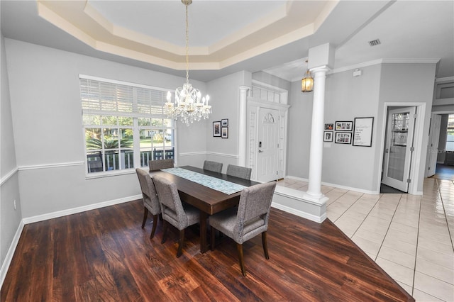 tiled dining room with decorative columns, a raised ceiling, crown molding, and a notable chandelier