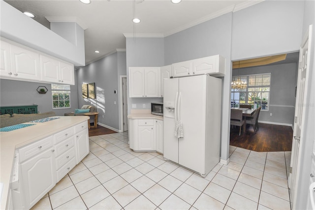 kitchen with white cabinets, a healthy amount of sunlight, white fridge with ice dispenser, and ornamental molding