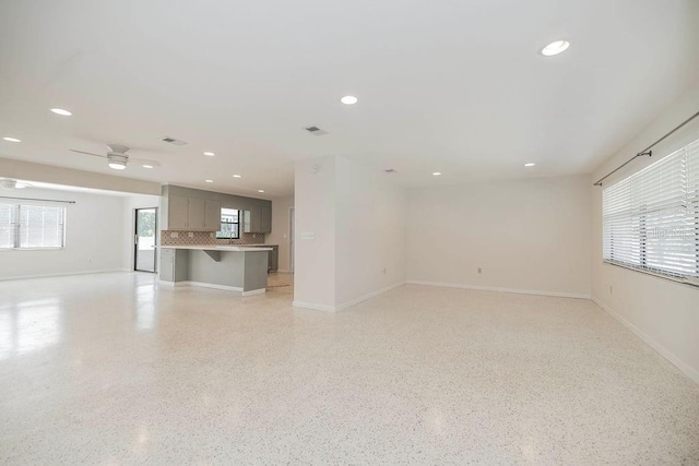 unfurnished living room with baseboards, visible vents, light speckled floor, and recessed lighting