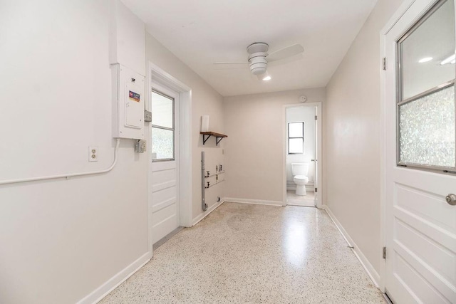 corridor with light speckled floor, electric panel, a healthy amount of sunlight, and baseboards