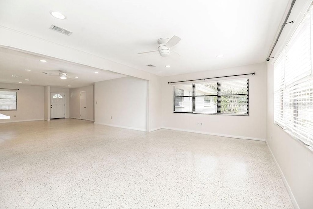 empty room with light speckled floor, visible vents, ceiling fan, and baseboards