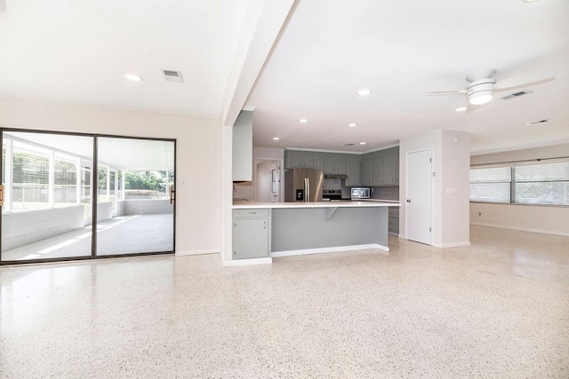 unfurnished living room with light speckled floor, visible vents, baseboards, and a ceiling fan