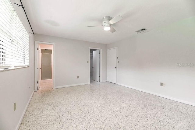 unfurnished bedroom featuring a walk in closet, visible vents, a ceiling fan, baseboards, and speckled floor