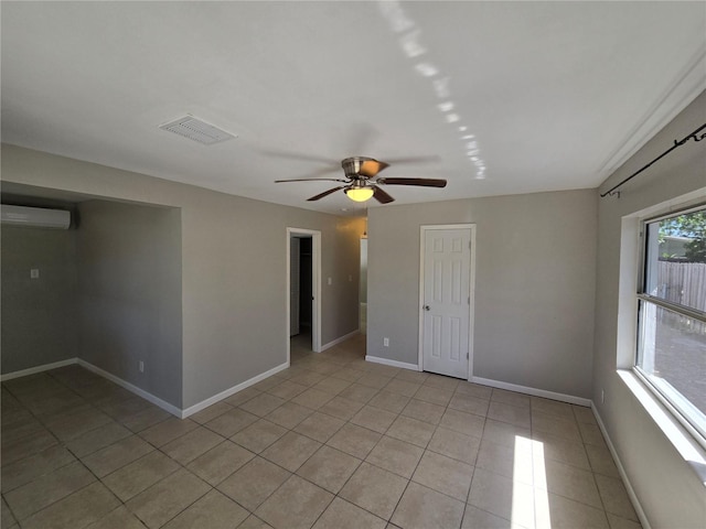 spare room featuring light tile patterned flooring, a wall unit AC, baseboards, visible vents, and ceiling fan