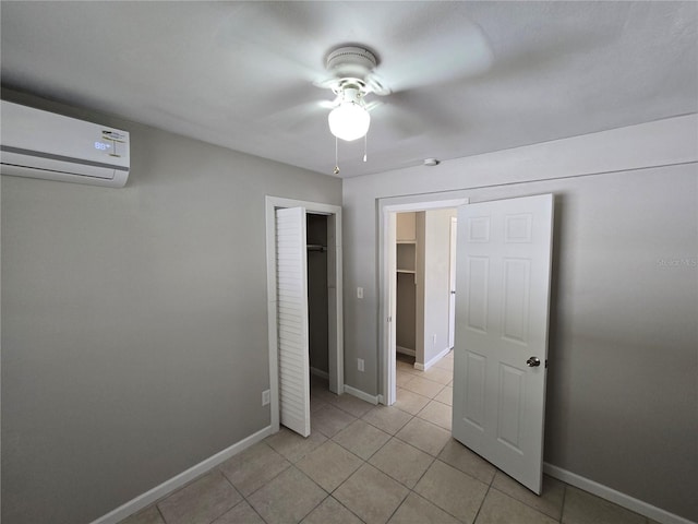 unfurnished bedroom with a wall mounted air conditioner, a closet, baseboards, a ceiling fan, and light tile patterned floors
