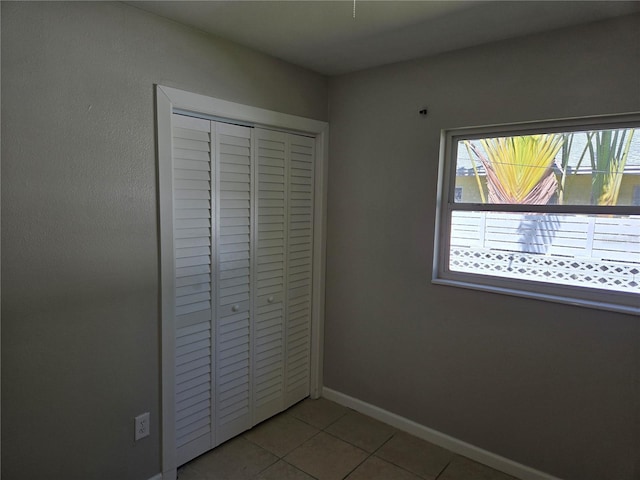 unfurnished bedroom featuring a closet, baseboards, and light tile patterned floors