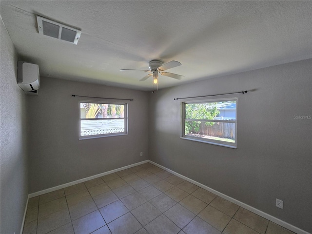 tiled empty room with ceiling fan, visible vents, a healthy amount of sunlight, and an AC wall unit