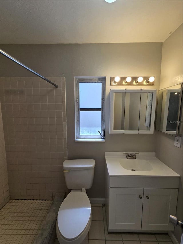bathroom with tile patterned flooring, vanity, a tile shower, toilet, and baseboards