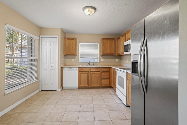 kitchen with a textured ceiling, white appliances, sink, and light tile patterned floors