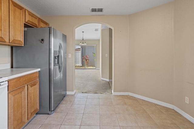 kitchen featuring an inviting chandelier, stainless steel refrigerator with ice dispenser, pendant lighting, a textured ceiling, and light tile patterned floors