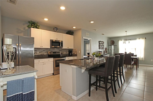 kitchen featuring a kitchen bar, appliances with stainless steel finishes, a kitchen island with sink, sink, and decorative light fixtures