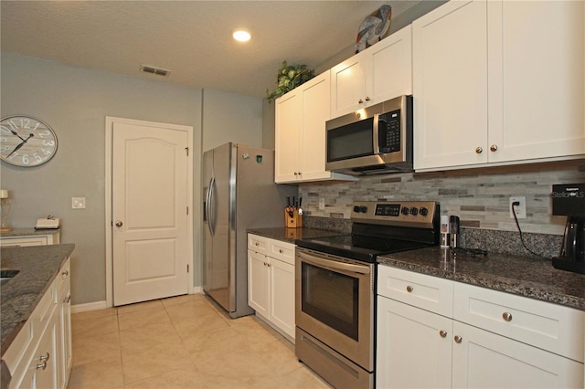 kitchen featuring appliances with stainless steel finishes, backsplash, dark stone counters, light tile patterned floors, and white cabinets