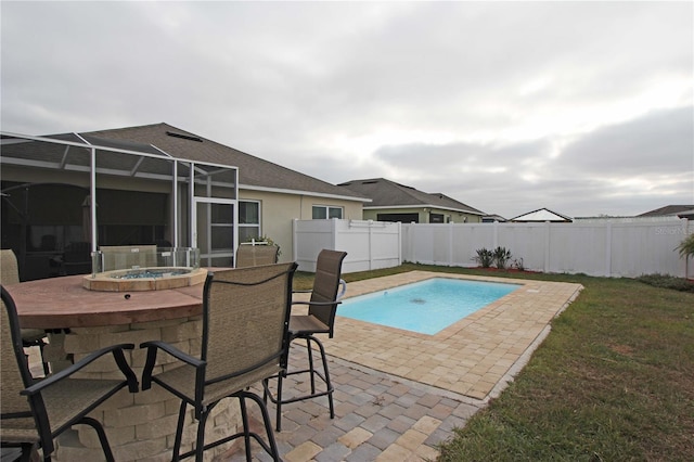 view of swimming pool with glass enclosure, a patio area, a yard, and an outdoor hot tub