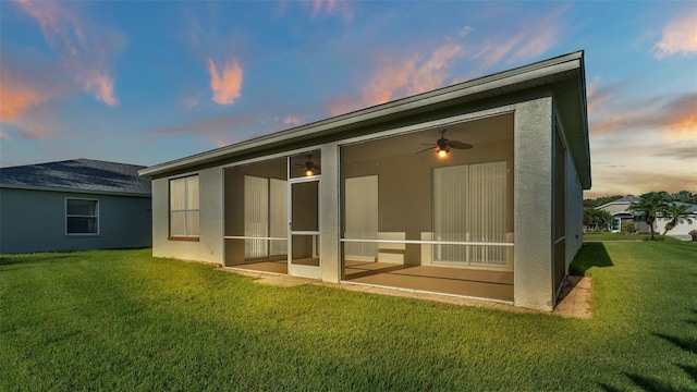 back house at dusk featuring a lawn and ceiling fan