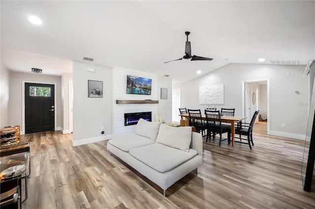 living room with vaulted ceiling, a large fireplace, ceiling fan, and light hardwood / wood-style floors