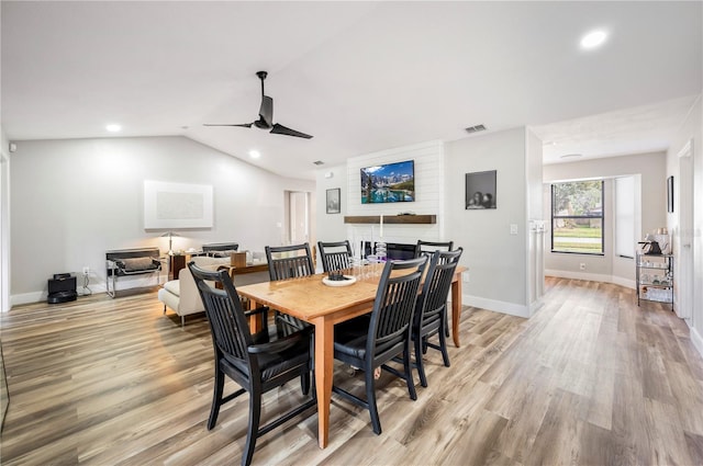 dining room with lofted ceiling, a large fireplace, ceiling fan, and light hardwood / wood-style flooring