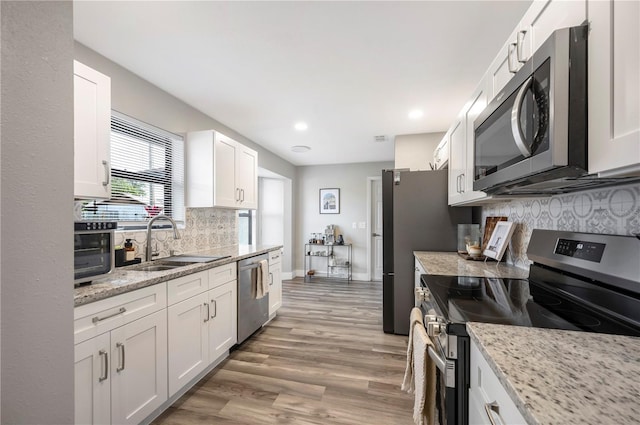 kitchen featuring white cabinetry, wood-type flooring, sink, light stone counters, and stainless steel appliances