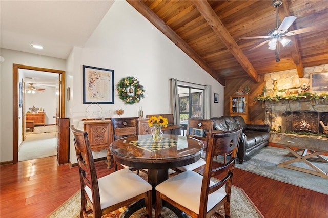 dining area featuring wood ceiling, ceiling fan, vaulted ceiling with beams, light hardwood / wood-style floors, and a stone fireplace