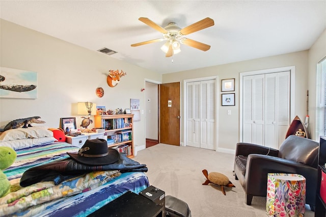 carpeted bedroom featuring ceiling fan and two closets