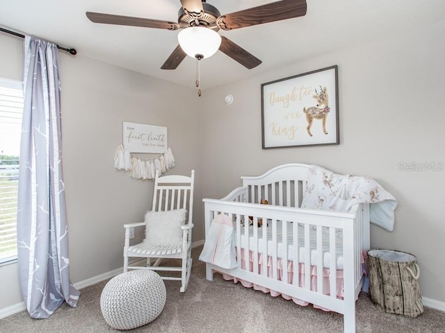 carpeted bedroom featuring multiple windows, a nursery area, and ceiling fan