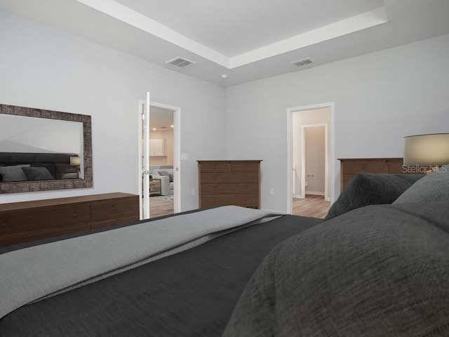 bedroom featuring a tray ceiling, connected bathroom, and light hardwood / wood-style flooring