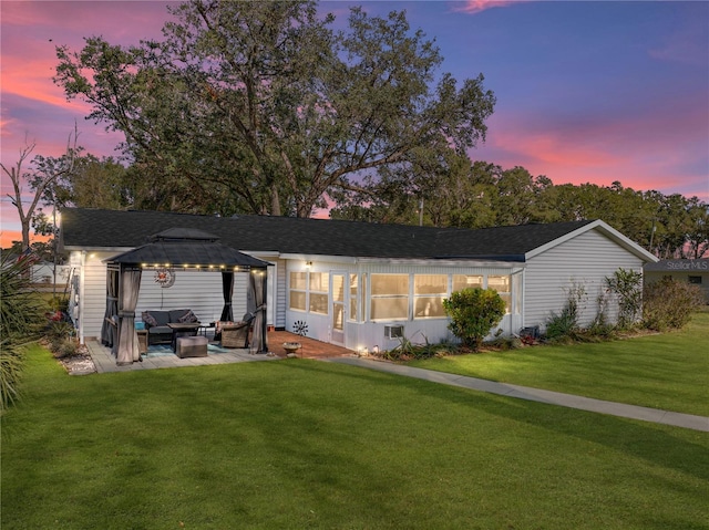 back house at dusk with outdoor lounge area, a gazebo, a patio area, and a lawn