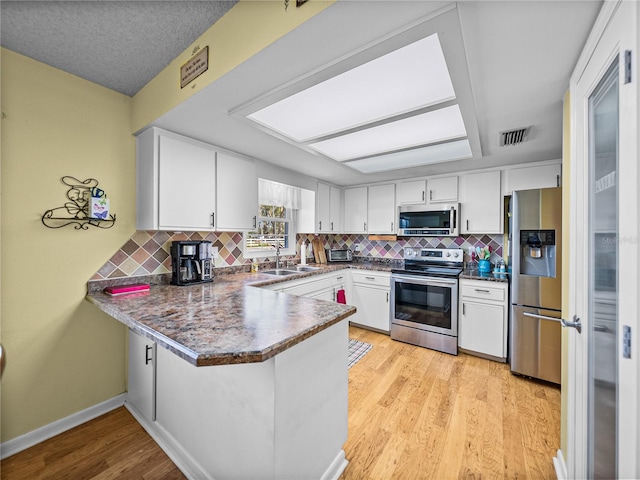 kitchen with sink, tasteful backsplash, kitchen peninsula, white cabinets, and appliances with stainless steel finishes