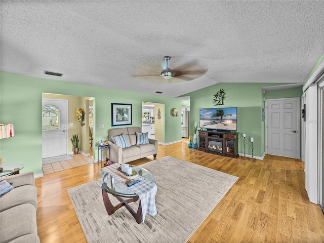 living room featuring a textured ceiling, vaulted ceiling, light hardwood / wood-style flooring, and ceiling fan