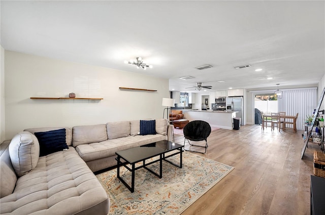 living room with ceiling fan with notable chandelier and light wood-type flooring