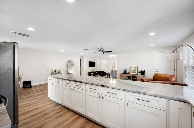 kitchen featuring light stone countertops, stainless steel fridge, ceiling fan, white cabinets, and light hardwood / wood-style floors