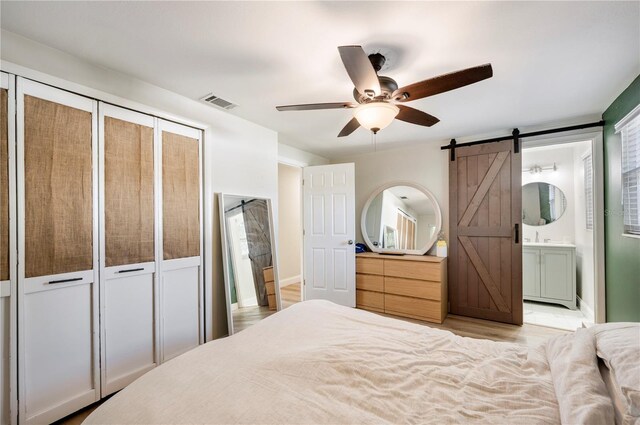 bedroom with a barn door, ensuite bathroom, a closet, and ceiling fan