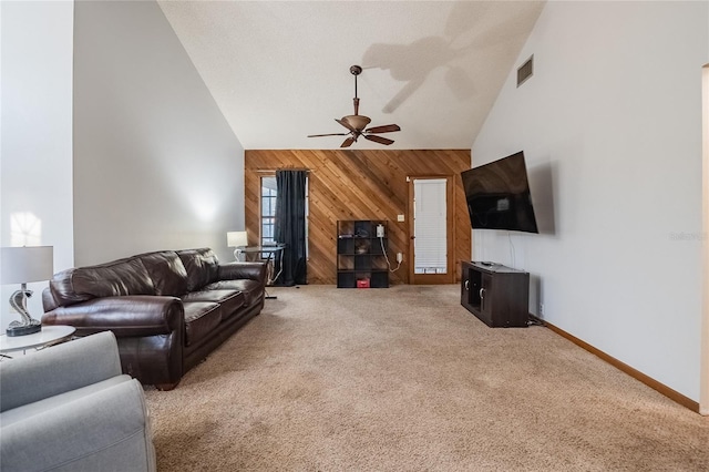 carpeted living room with wood walls, ceiling fan, and high vaulted ceiling