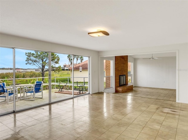 unfurnished living room with a brick fireplace, light tile patterned flooring, ceiling fan, and plenty of natural light