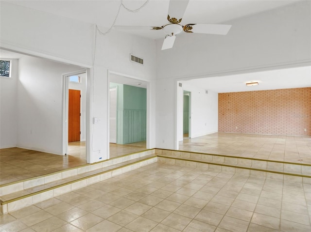 empty room featuring brick wall, high vaulted ceiling, ceiling fan, and light tile patterned floors